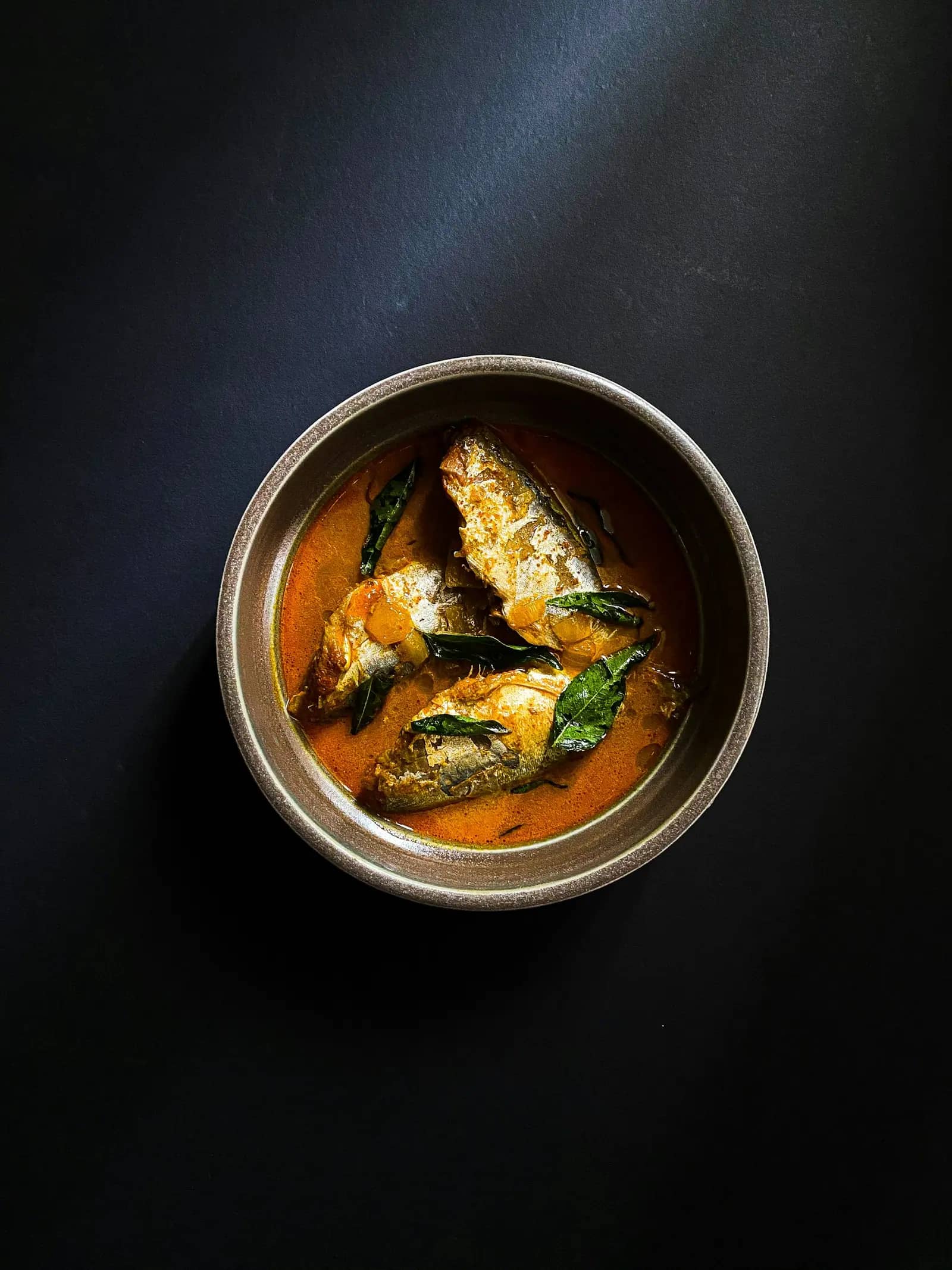 Fish curry in a steel bowl on a dark table