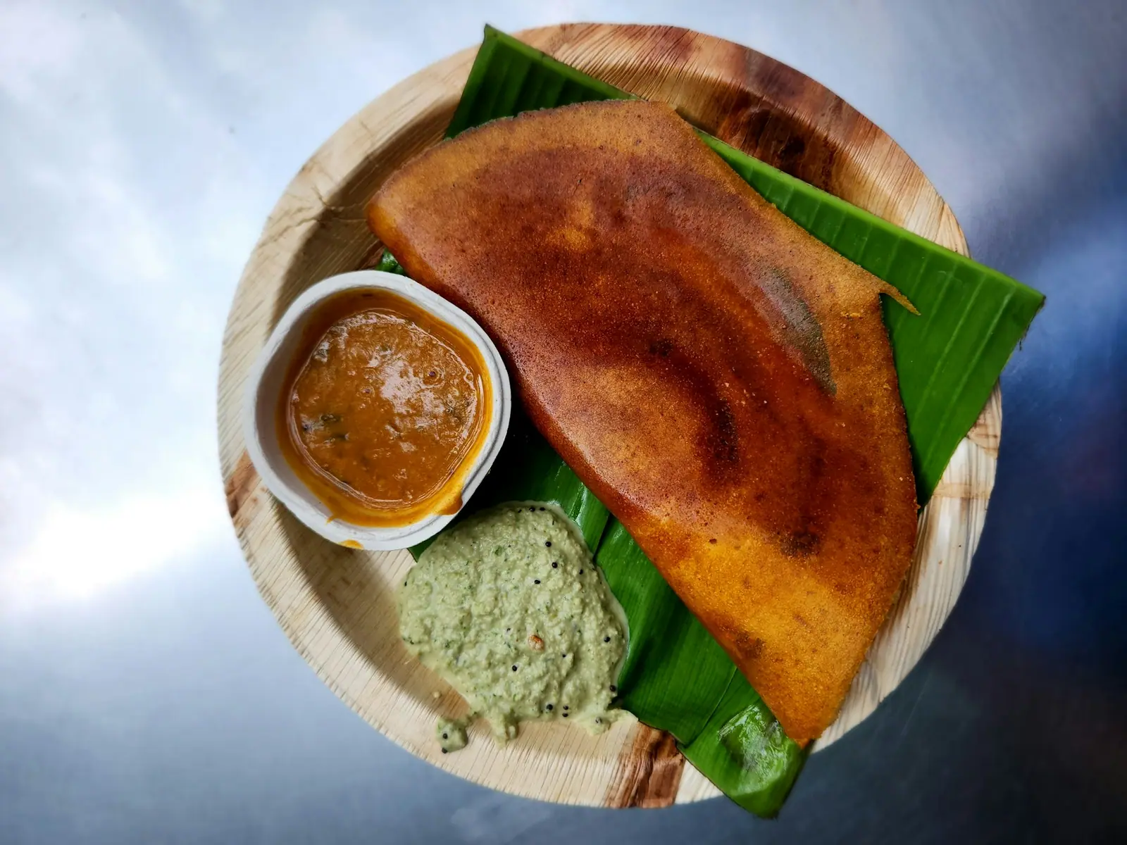 Golden dosa with coconut chutney and sambar on a banana leaf plate