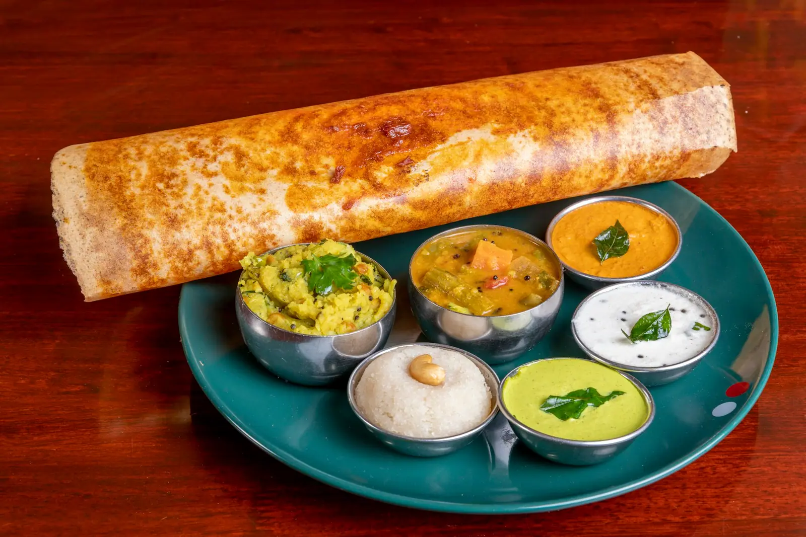 Crisp dosa with sambar and chutneys on a red table